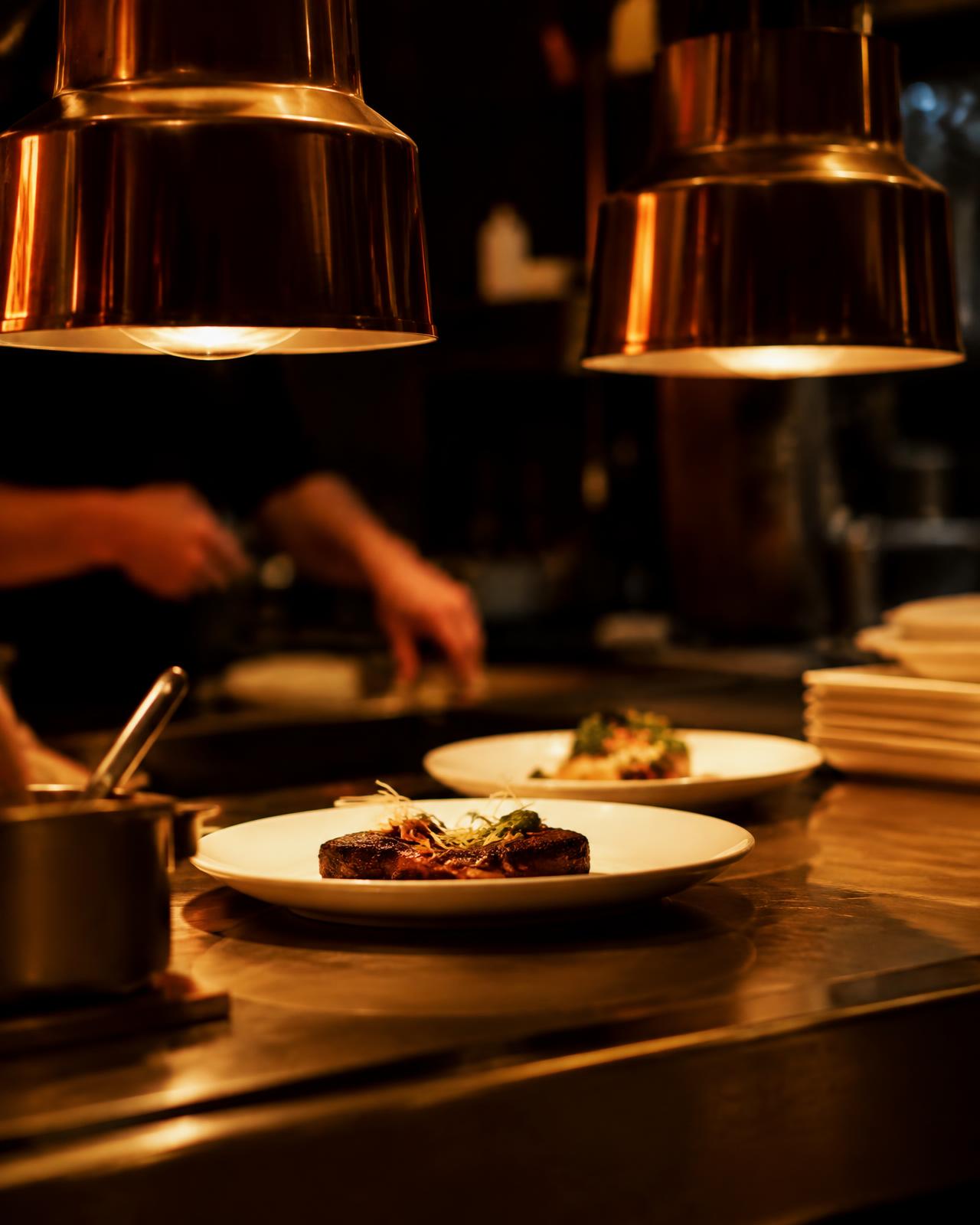 Plates waiting under heat lamps at a restaurant kitchen pass